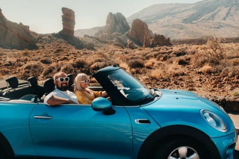 a woman and a man wearing glasses in a convertible car on a trip to the island of Tenerife. The