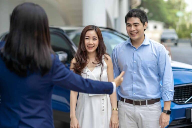 Asian Saleswoman welcoming the couple customer to checking the car infront of showroom