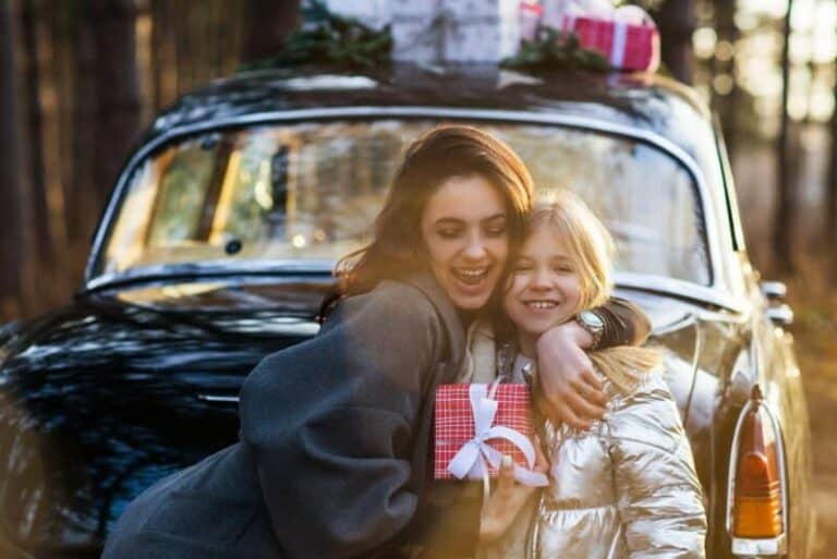 Happy woman with daughter standing next to car with Christmas gifts