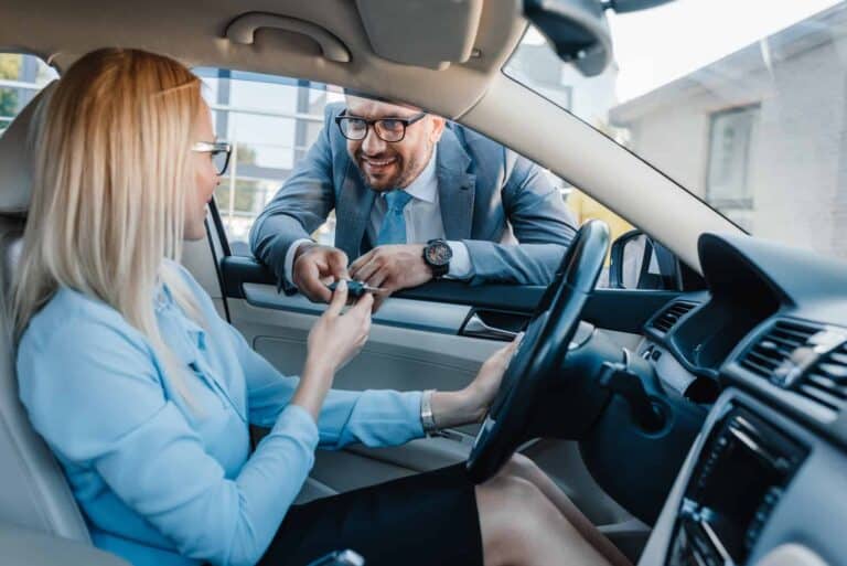 smiling businessman giving car keys to colleague at driver seat in car