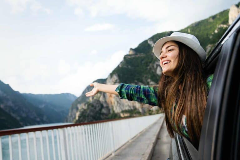 Woman in car road trip waving out the window smiling